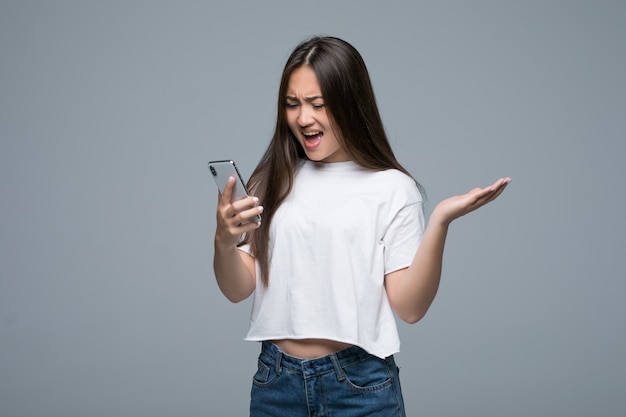 Vue latérale d'une femme asiatique tenant un smartphone et regardant en arrière sur fond gris