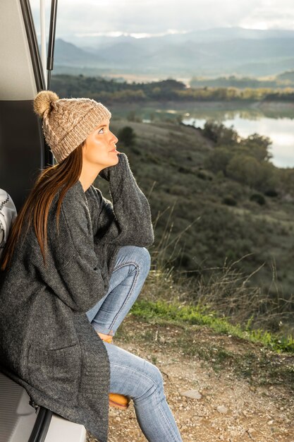 Vue latérale d'une femme assise sur le coffre de la voiture lors d'un voyage sur la route