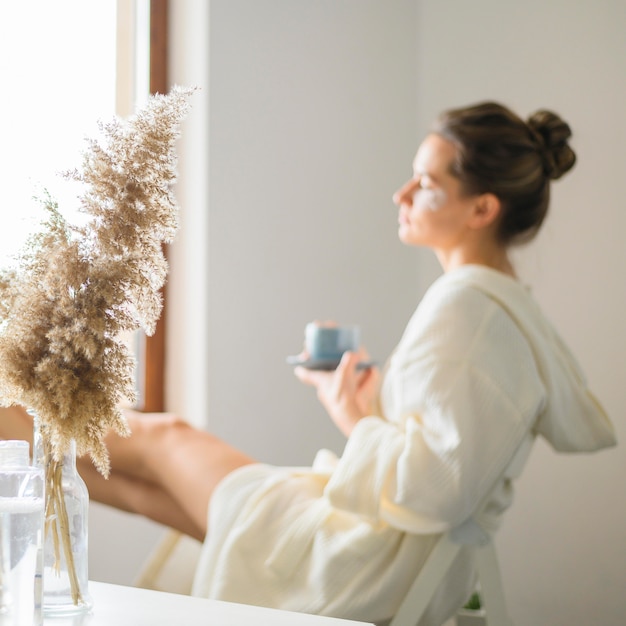 Vue latérale d'une femme défocalisée bénéficiant d'une journée de spa à la maison tout en buvant un café