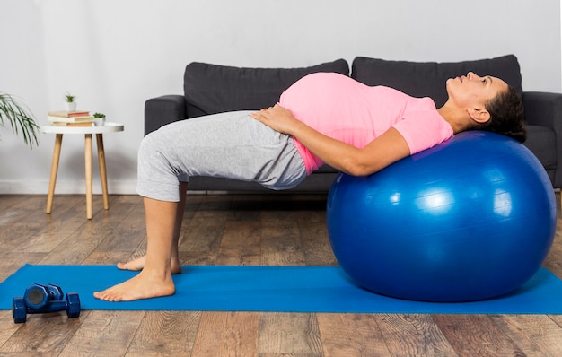 Vue latérale d'une femme enceinte à l'aide de ballon pour faire de l'exercice à la maison