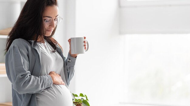 Vue latérale d'une femme enceinte à la maison avec une tasse de café