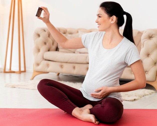 Vue latérale d'une femme enceinte en position du lotus prenant un selfie