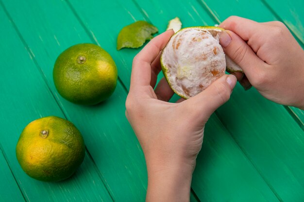 Photo gratuite vue latérale femme épluche la peau de mandarine sur le mur vert