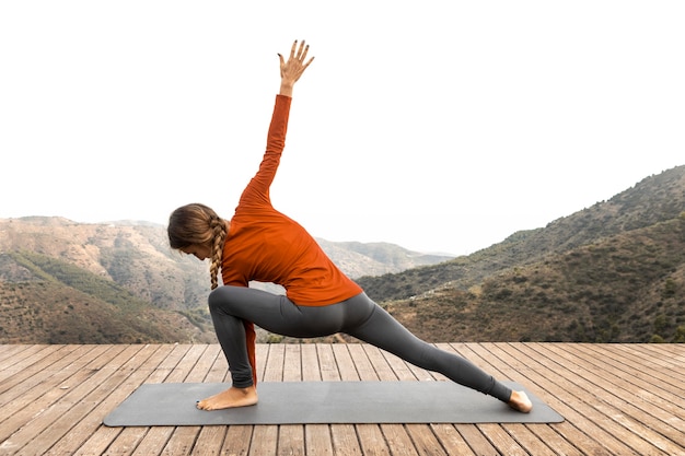 Vue latérale de la femme à l'extérieur dans la nature, faire du yoga sur tapis