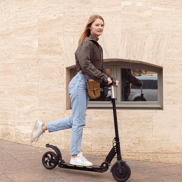 Vue latérale de la femme à l'extérieur avec scooter électrique