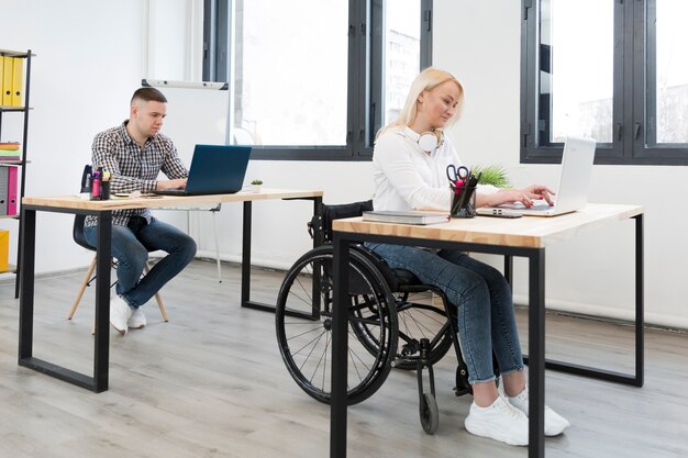 Vue latérale d'une femme en fauteuil roulant travaillant sur son bureau