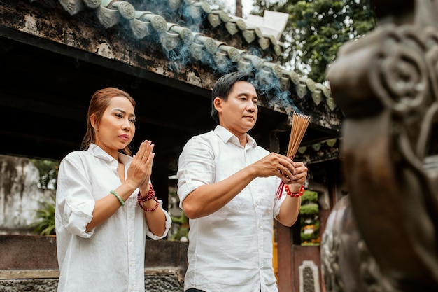 Vue latérale de la femme et de l'homme priant au temple avec de l'encens brûlant