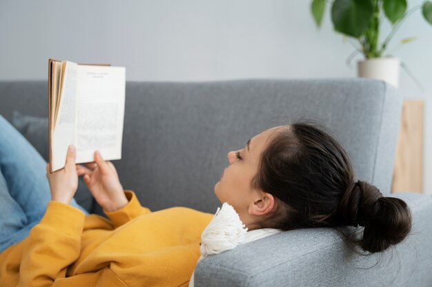 Vue latérale femme lisant sur le canapé