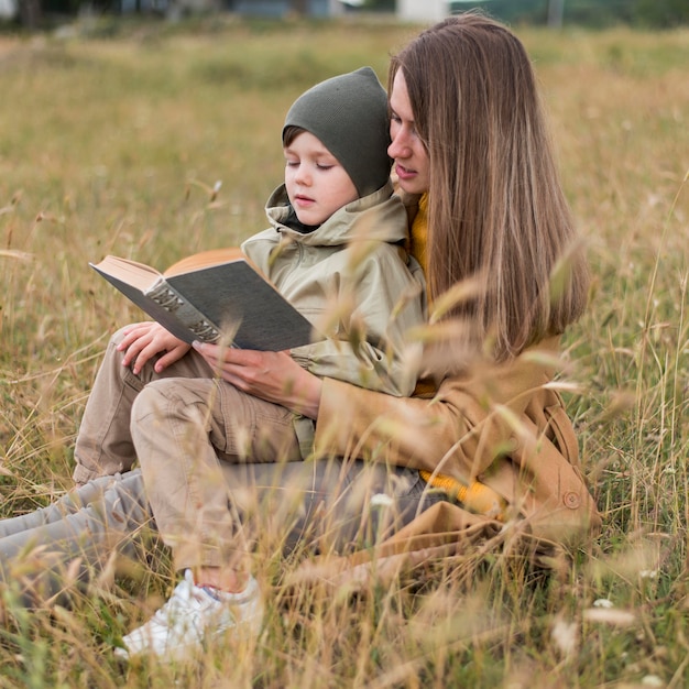Vue latérale femme lisant un livre à son fils à l'extérieur