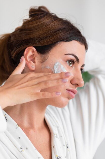 Vue latérale d'une femme magnifique à l'aide de crème