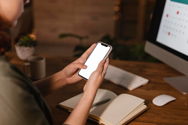 Vue latérale de la femme à la maison à l'aide de son smartphone devant son ordinateur