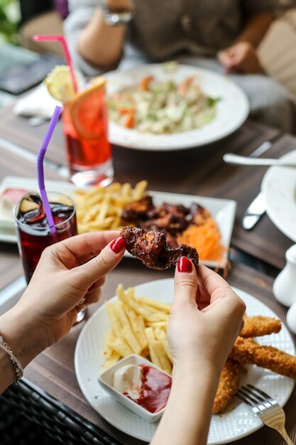 Vue latérale femme mange des ailes de barbecue avec des frites et du ketchup avec de la mayonnaise sur une assiette