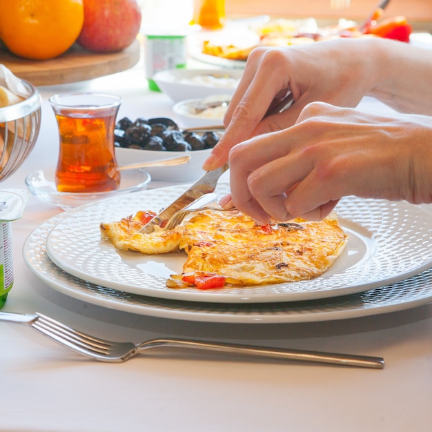 Photo gratuite vue latérale femme mangeant une omelette dans la cuisine avec du thé, des olives, des fruits en arrière-plan.