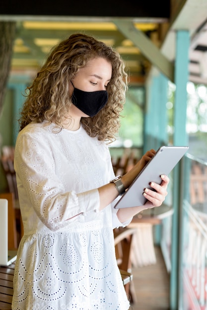 Photo gratuite vue latérale femme avec masque à l'aide de tablette