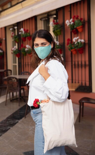 Vue latérale d'une femme avec un masque facial et des sacs d'épicerie à l'extérieur