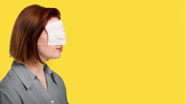 Photo gratuite vue latérale femme avec masque sur les yeux debout à côté du mur éclairant