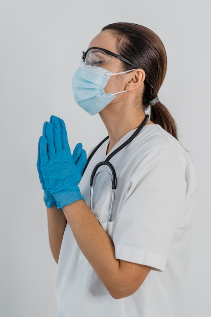 Vue latérale d'une femme médecin avec masque médical et lunettes de sécurité priant