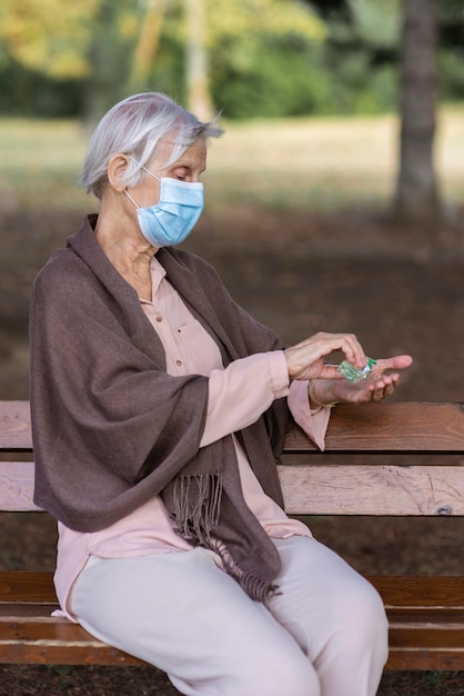 Vue latérale d'une femme plus âgée avec masque médical et désinfectant pour les mains