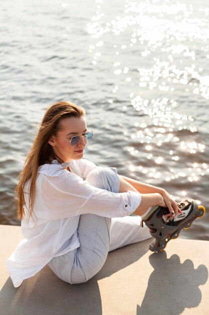 Vue latérale d'une femme posant au bord du lac avec des patins à roulettes