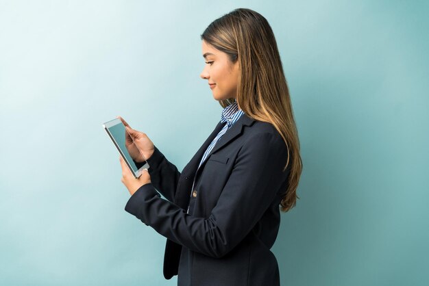 Vue latérale d'une femme professionnelle regardant une tablette numérique en se tenant debout sur un fond coloré