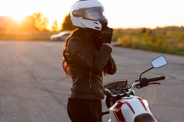 Vue latérale de la femme qui décolle son casque à côté de la moto