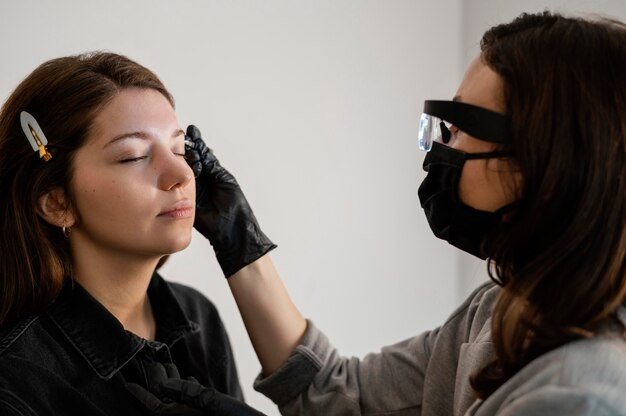 Vue latérale d'une femme qui reçoit un traitement des sourcils par une esthéticienne