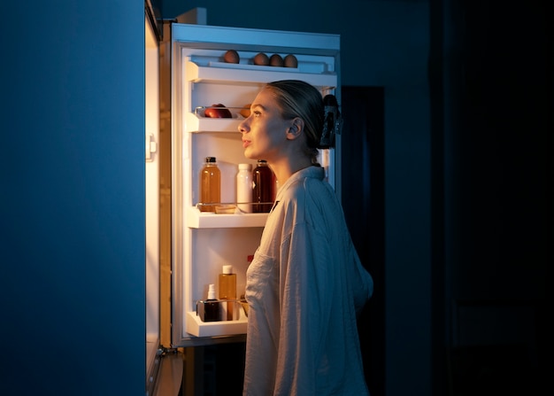 Vue latérale femme regardant dans le réfrigérateur