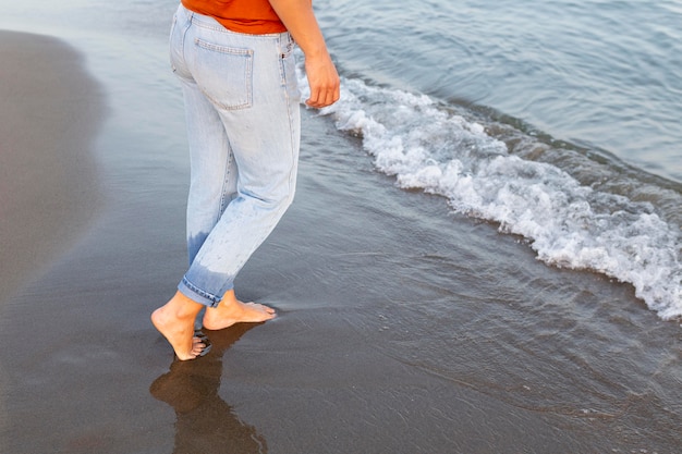 Vue latérale d'une femme se mettre les pieds dans l'eau à la plage