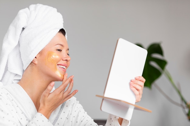 Vue latérale d'une femme souriante en peignoir appliquant des soins de la peau