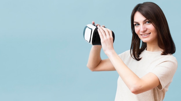 Vue latérale d'une femme souriante tenant un casque de réalité virtuelle