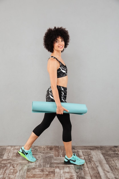 Photo gratuite vue latérale d'une femme sportive heureuse marchant avec un tapis de fitness