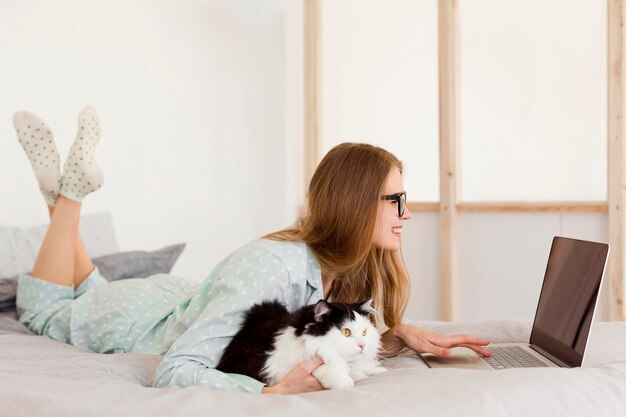 Vue latérale d'une femme travaillant en pyjama à la maison avec un chat