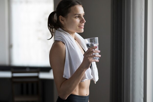 Vue latérale de la femme avec un verre d'eau et une serviette sur les épaules