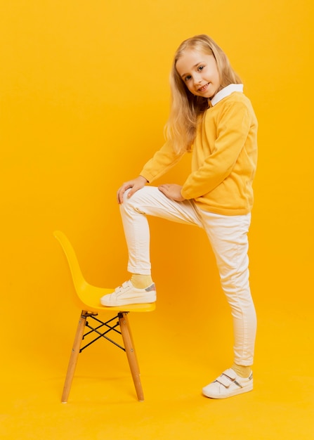 Vue latérale d'une fille heureuse posant avec une chaise