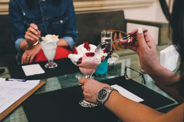 Vue latérale des filles mangent de la crème glacée dans un verre avec des fraises