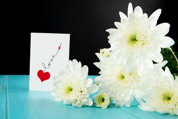 Vue latérale des fleurs de chrysanthème de couleur blanche et une carte postale sur fond de bois bleu