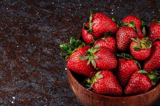 Vue latérale fraise dans un bol en bois sur fond noir