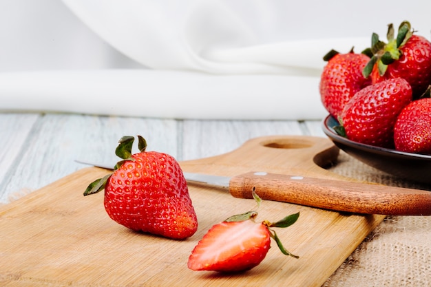 Vue latérale de la fraise fraîche sur un couteau et une planche sur fond blanc