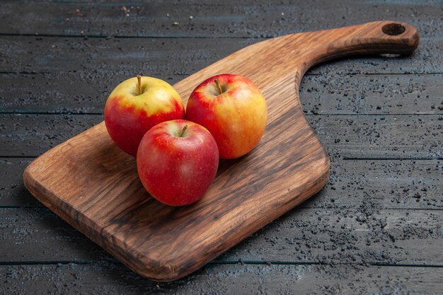 Vue latérale des fruits à bord de trois pommes jaune-rougeâtre sur une planche à découper marron sur une table grise