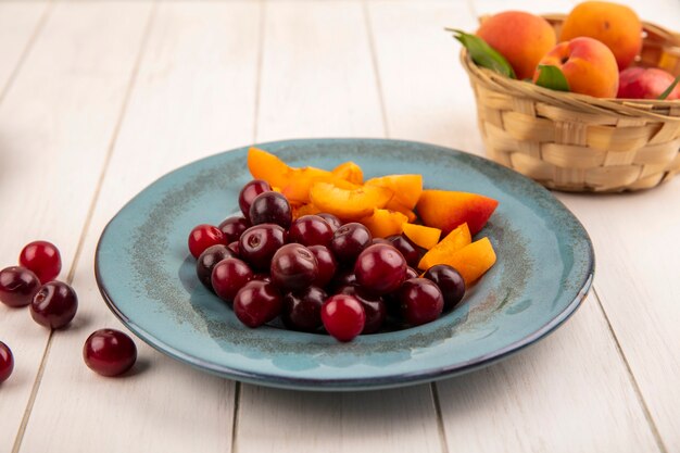 Vue latérale des fruits comme les cerises et les tranches d'abricot en assiette et panier d'abricots sur fond de bois