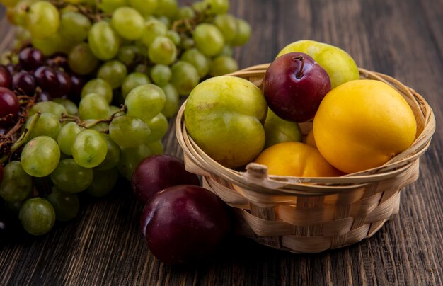 Vue latérale des fruits comme des nectacots verts et saveur king pluots dans le panier avec des raisins sur fond de bois