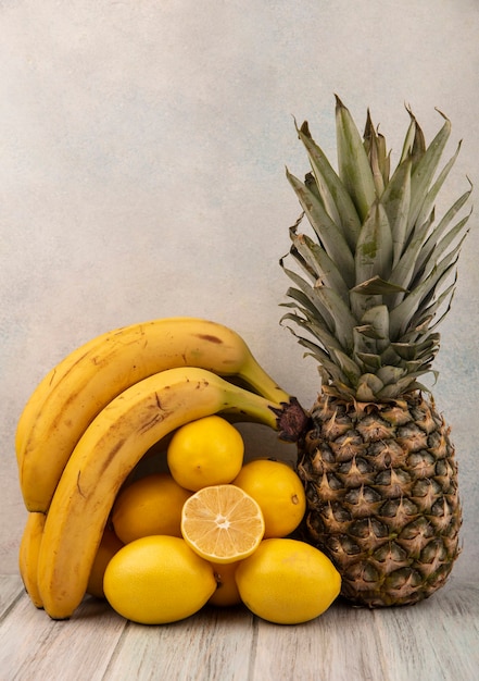 Photo gratuite vue latérale de fruits frais et savoureux tels que les bananes, les citrons et l'ananas isolé sur une table en bois gris sur fond blanc