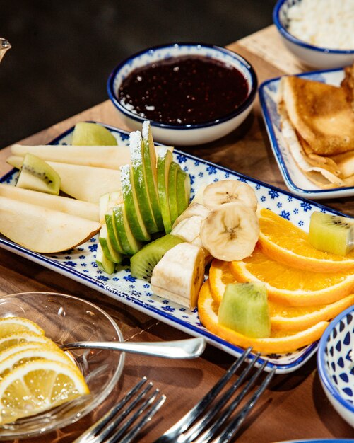 Vue latérale de fruits frais en tranches bananes pommes kiwi et orange sur le plateau