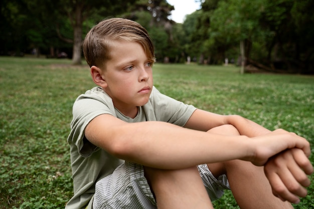 Photo gratuite vue latérale garçon triste assis sur l'herbe