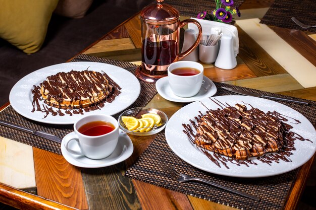 Photo gratuite vue latérale de la gaufre aux bananes recouvertes de chocolat sur une plaque blanche servie avec du thé sur la table