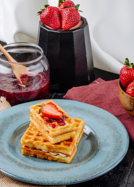 Vue latérale des gaufres à la crème à la vanille et à la confiture de fraises sur la table