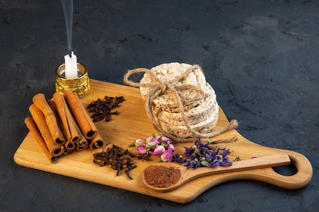 Vue latérale des gousses d'épices avec des bâtons de cannelle, des pains de riz attachés avec une corde rose thé et bougie sur planche de bois