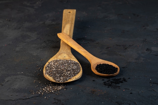 Vue latérale des graines de cumin noir dans des cuillères en bois sur fond noir