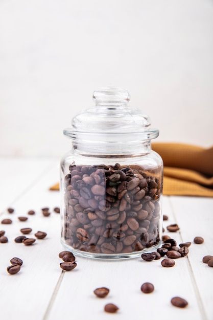Photo gratuite vue latérale des grains de café torréfiés frais sur un bocal en verre sur un fond en bois blanc
