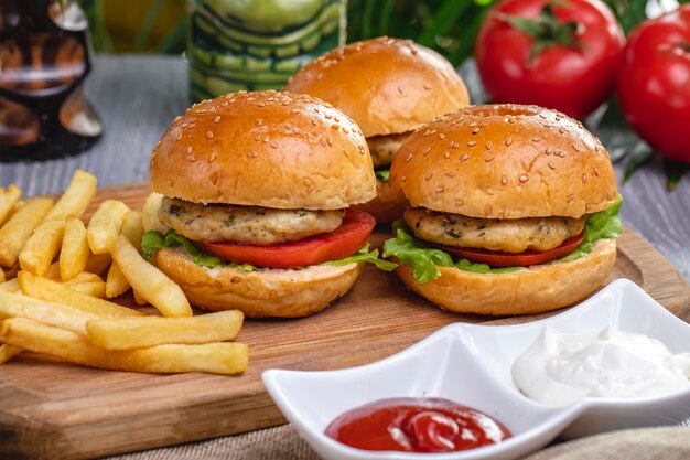 Vue latérale des hamburgers de poulet avec du ketchup de frites et de la mayonnaise sur la planche